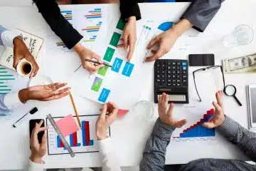 People's hands are seen collaborating on financial charts and documents at a white table, with a calculator, glasses, money, and pencils—clearly showcasing the meticulous work of a Chartered Accountants Team. KGRN Chartered Accountants in Dubai offers a comprehensive range of services including audit and assurance, accounting and bookkeeping, tax consulting and compliance, business advisory, corporate finance, management consulting, internal audit, forensic accounting, company formation, and legal and secretarial services. Each service is tailored to support businesses in managing their financial operations effectively and ensuring compliance with regulatory requirements.