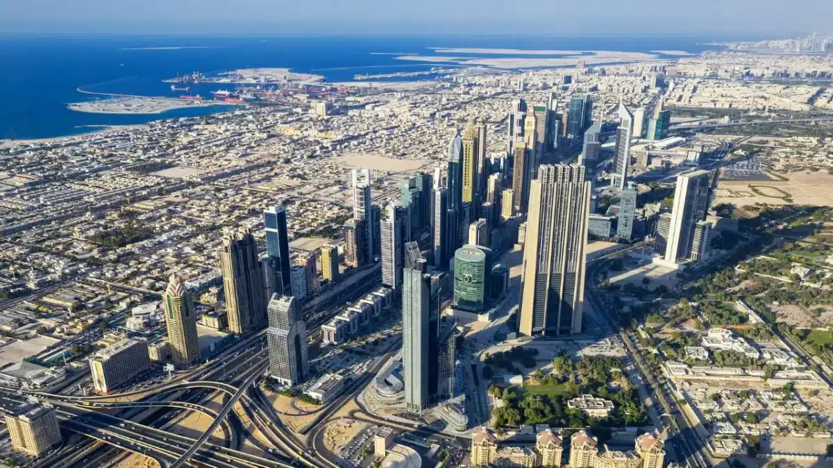 Aerial view of a city with numerous high-rise buildings and skyscrapers clustered together, surrounded by a network of roads and highways. The cityscape extends towards the coastline, with sandy beaches and blue waters visible in the background—a testament to the benefits of Free Zone Company Formation.